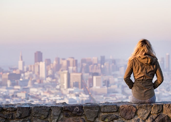 young girl sitting on wall overlooking big city